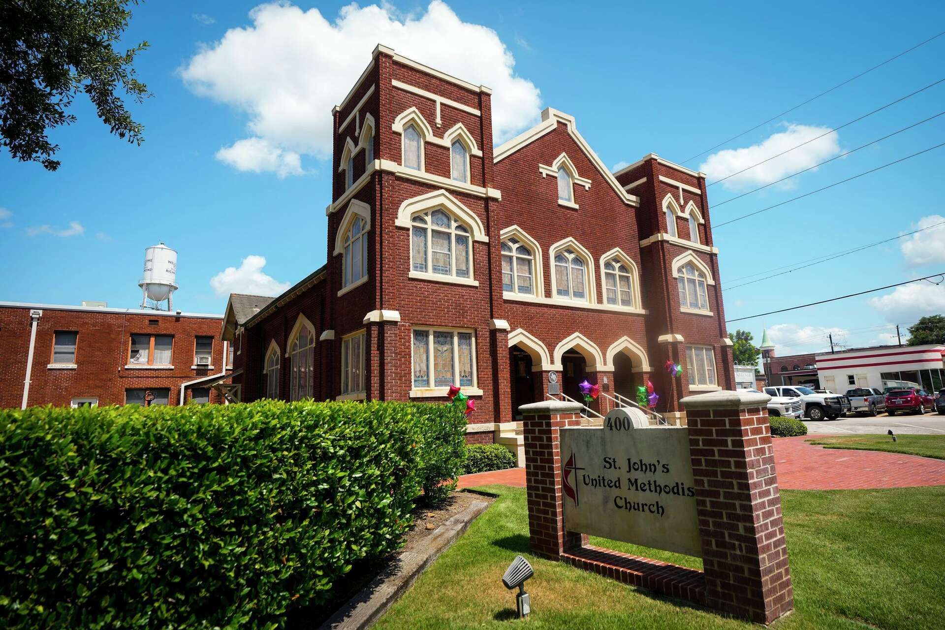 Red brick historic building with white trim and a sign at the entrance under a blue sky.