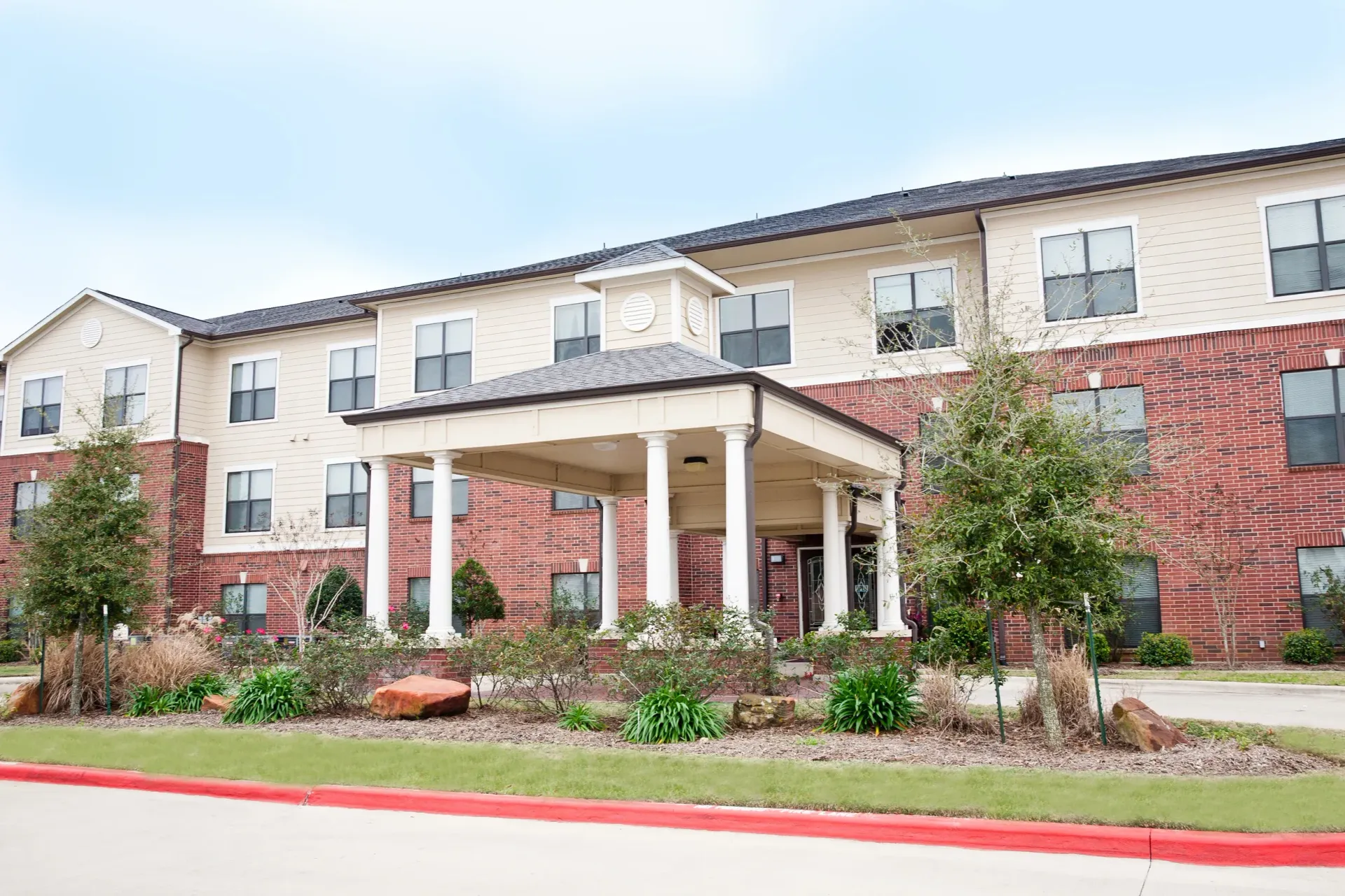 Apartment building entrance with red brick and beige siding, covered walkway, and landscaped front lawn