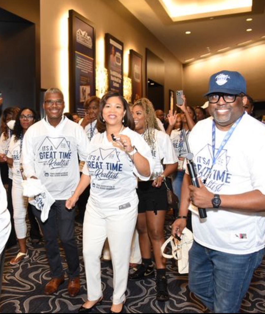 Courtney, with smiling attendees in white event T-shirts, poses in a hotel hallway.