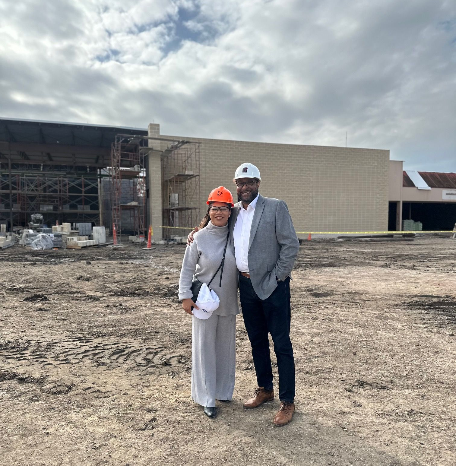 Courtney and a colleague in hard hats stand outside a construction site under a cloudy sky.