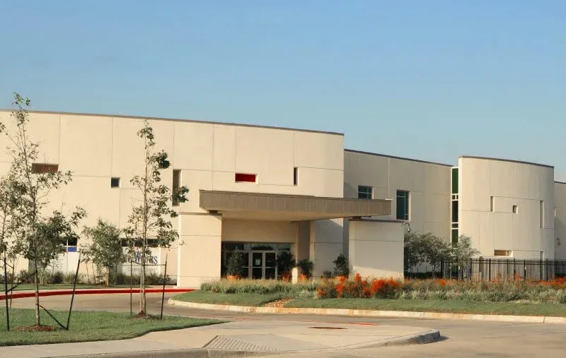 Modern beige building with curved walls, entrance canopy, and landscaping under a clear sky