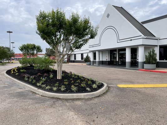 Building with a white facade, landscaped island, and parking lot entrance under a cloudy sky