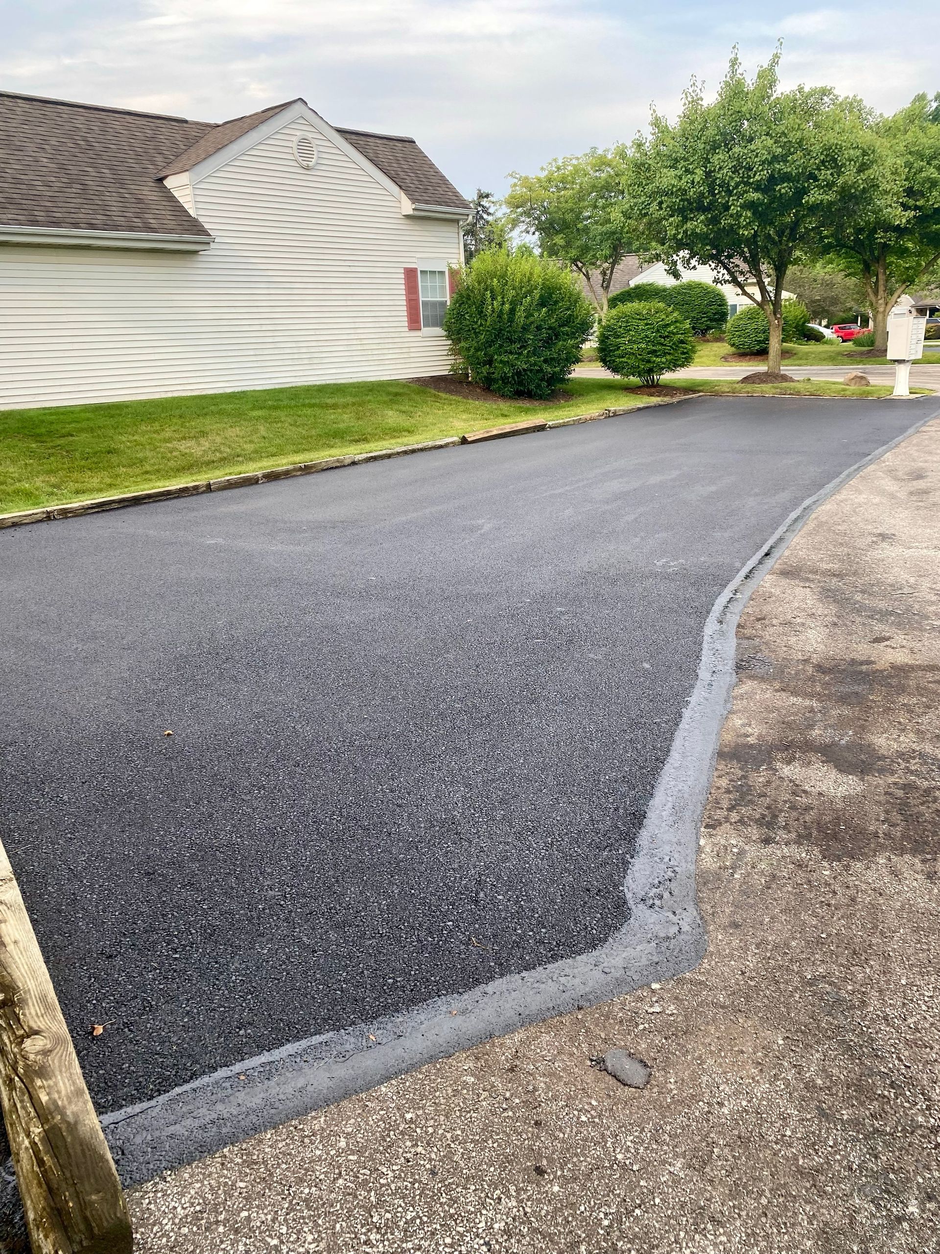 Freshly paved asphalt driveway with a curb, in front of a house, on a cloudy day.