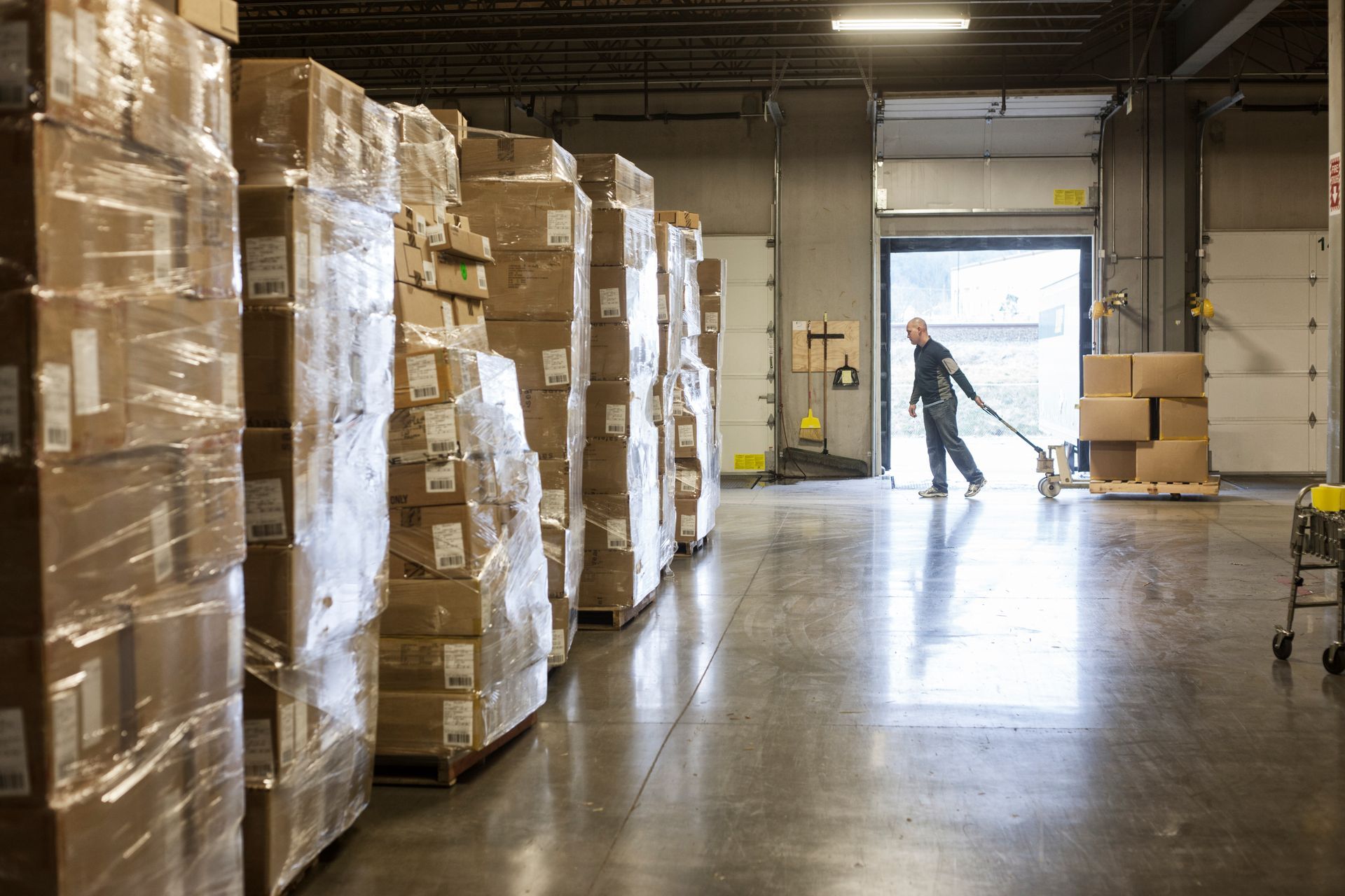 A man is pushing a cart in a warehouse filled with boxes