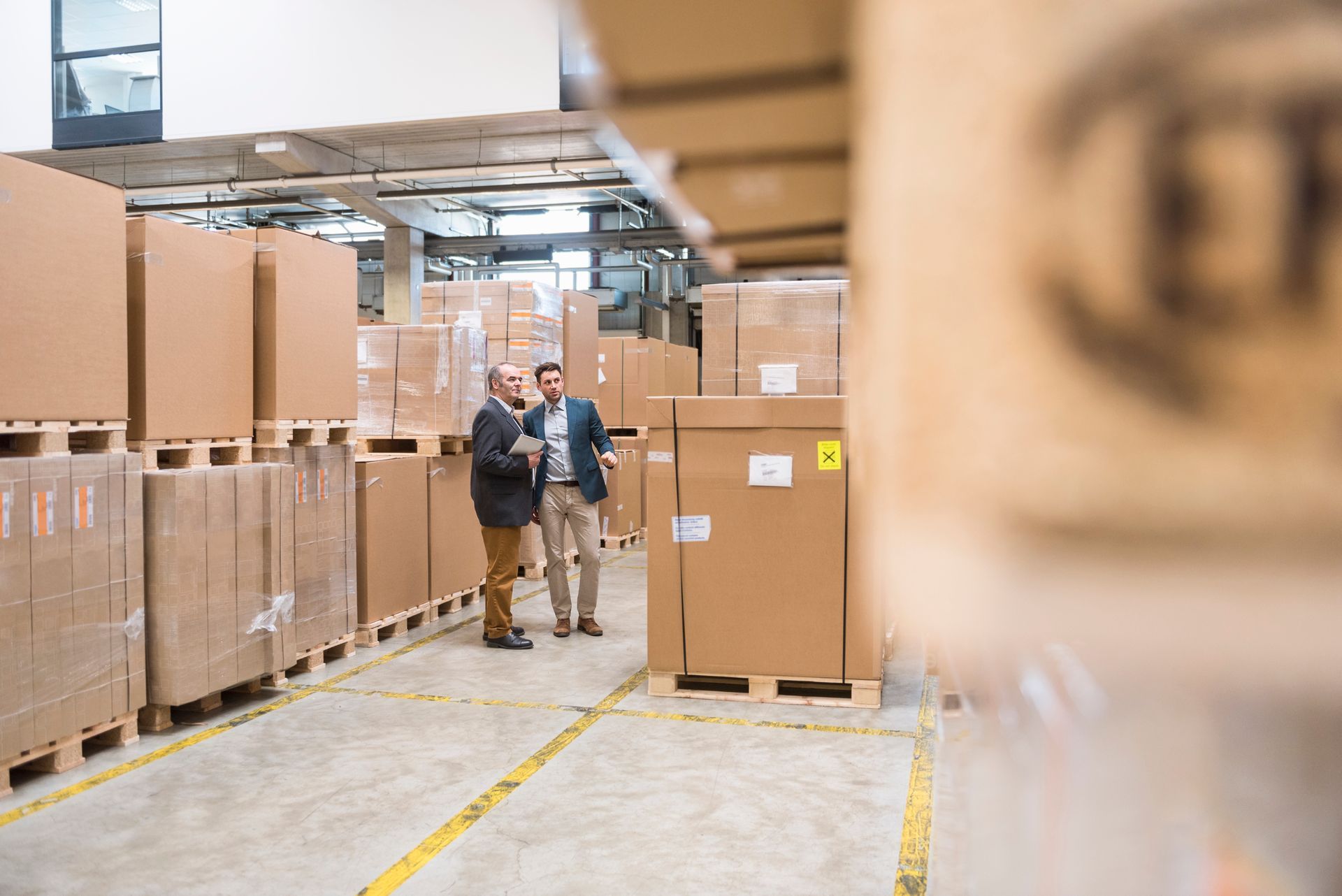 Two men are standing in a warehouse looking at a tablet.