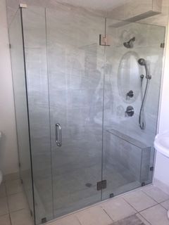 Glass shower enclosure with gray marble-look walls, chrome fixtures, and a bench.