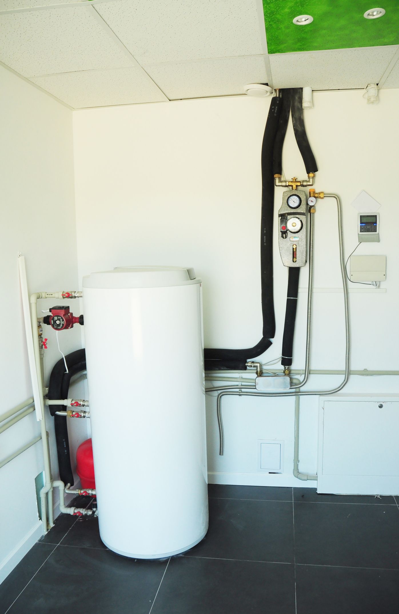 White water heater and pipes in a small room with a black floor and white walls.