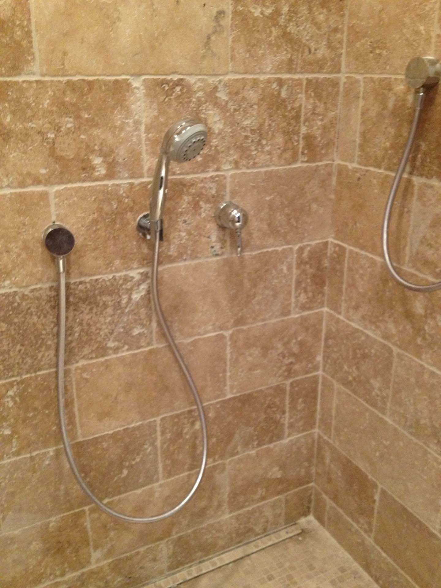 Shower with travertine tile walls and two handheld shower heads.