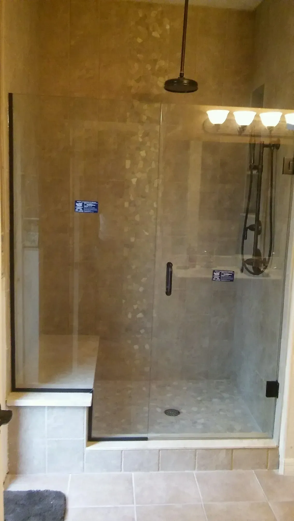Glass shower with a built-in bench, dark fixtures, and tiled walls.
