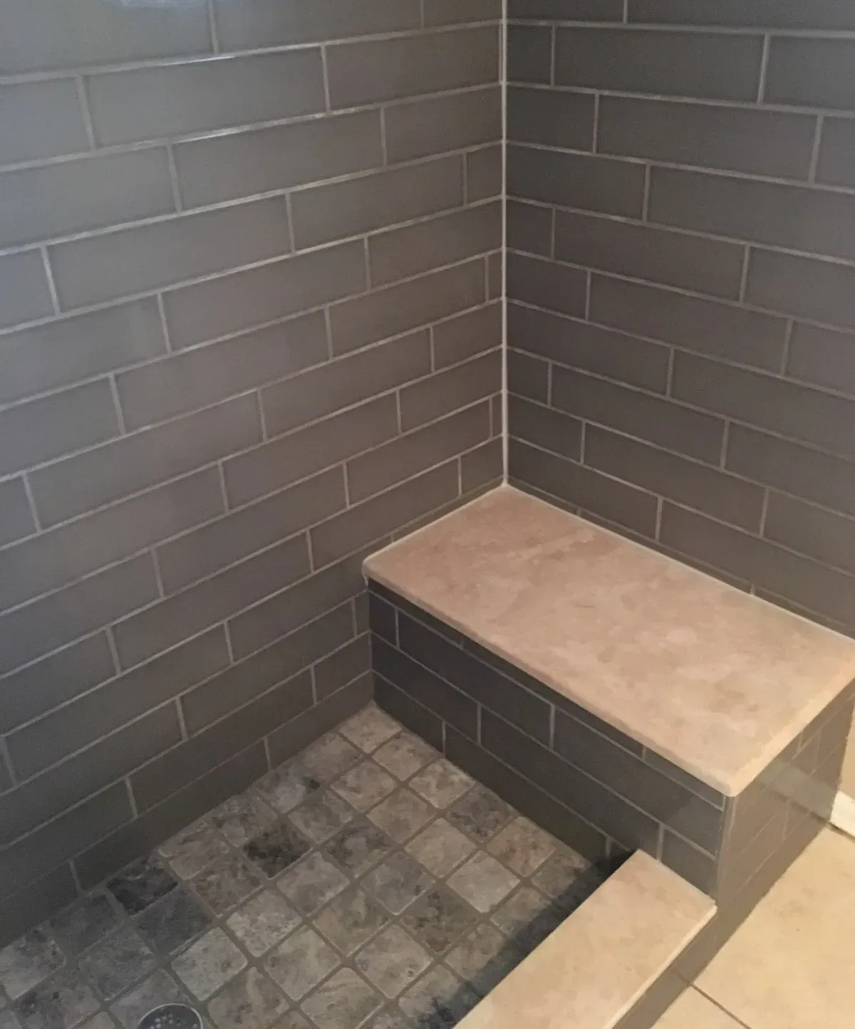 Gray tiled shower with a built-in seat. The floor tiles are darker.