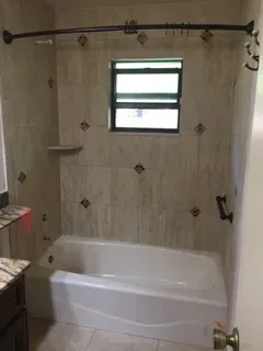 Bathroom with white tub, tiled walls with decorative accents, and a window.