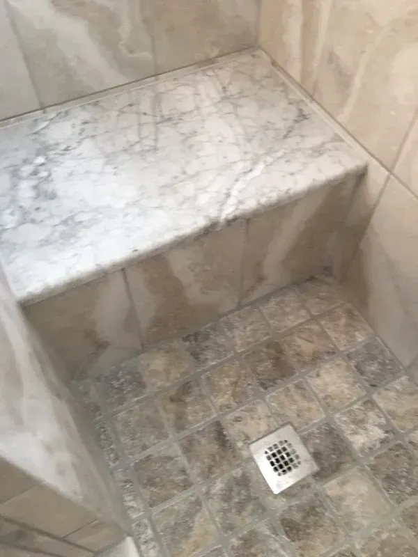 Shower interior with a marble bench and tile floor and walls.