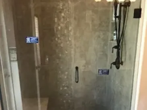 Shower with glass door, water stains. Dark fixtures, gray tile walls. Two small items attached to glass.