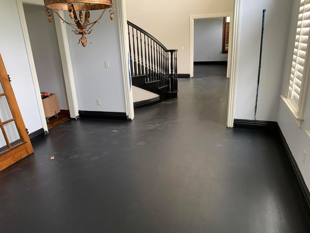 Empty living room with dark gray floor, staircase, and white walls leading to a hallway