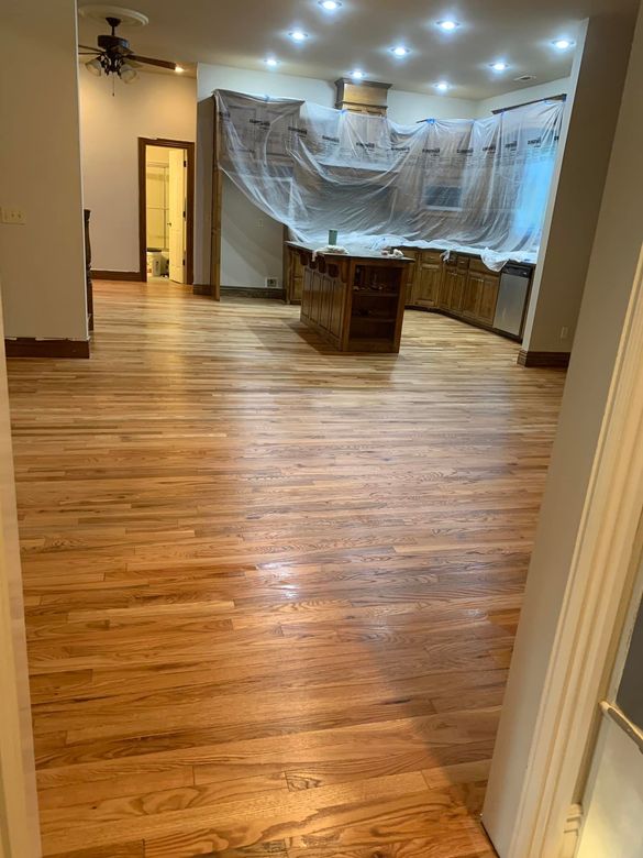 Empty kitchen under renovation with wood floors and plastic-covered cabinets, viewed from the doorway