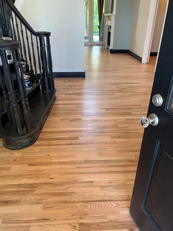 Hallway with light wood floor, black staircase railing, and open front door