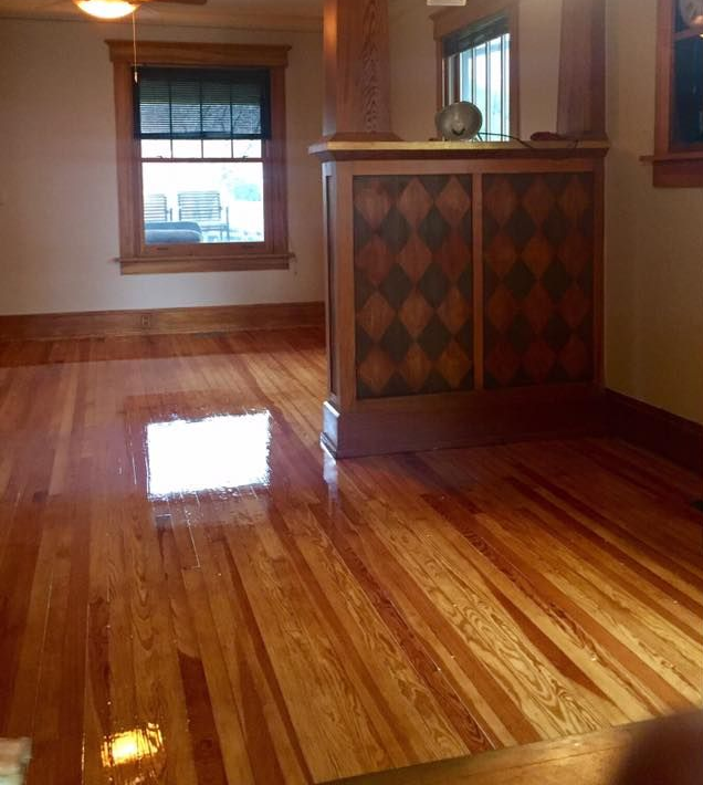 Empty polished hardwood room with windows, a radiator, and a decorative wooden counter.