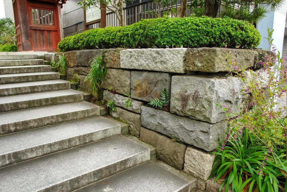 Stone stairway beside a landscaped retaining wall and garden greenery outside a house