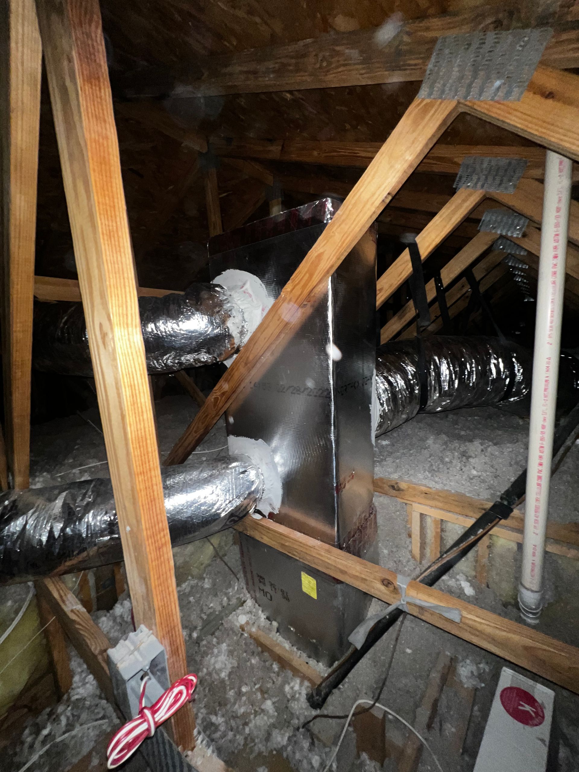 Attic crawlspace with exposed wooden beams and insulated silver HVAC ducts running through it