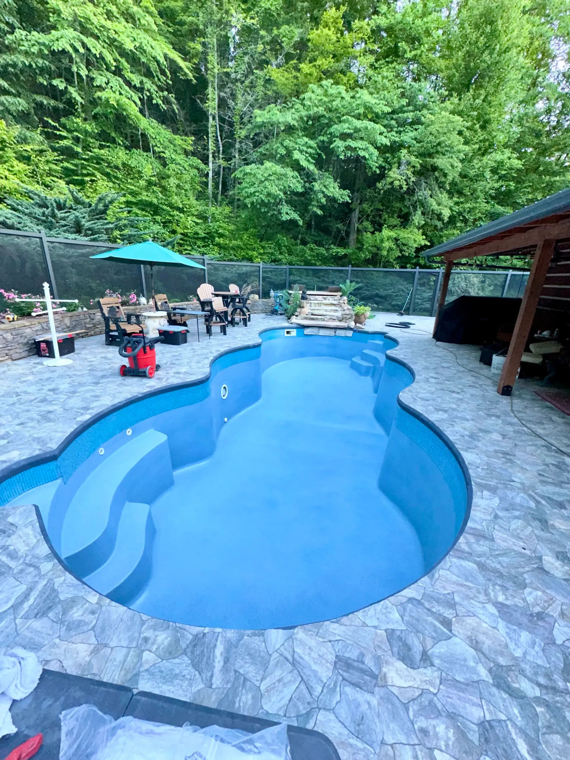 A large swimming pool in the backyard of a house surrounded by trees.
