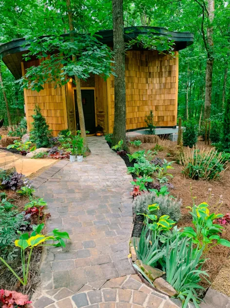 A small house in the middle of a forest with a stone walkway leading to it.