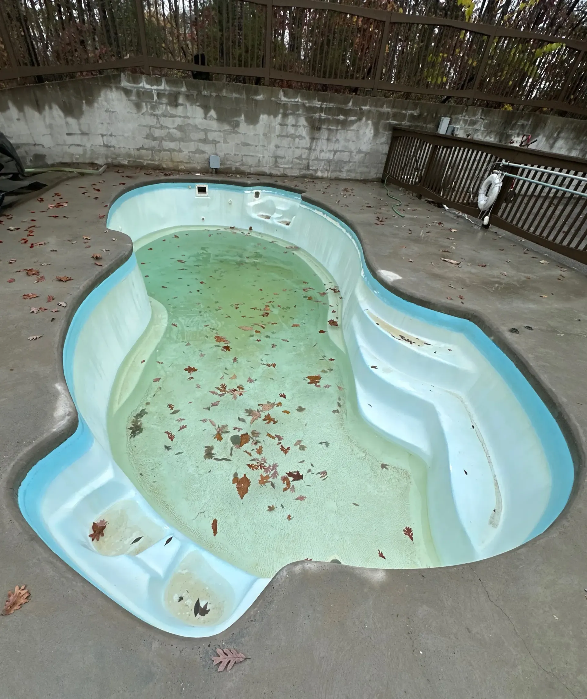 An empty swimming pool with leaves on the ground