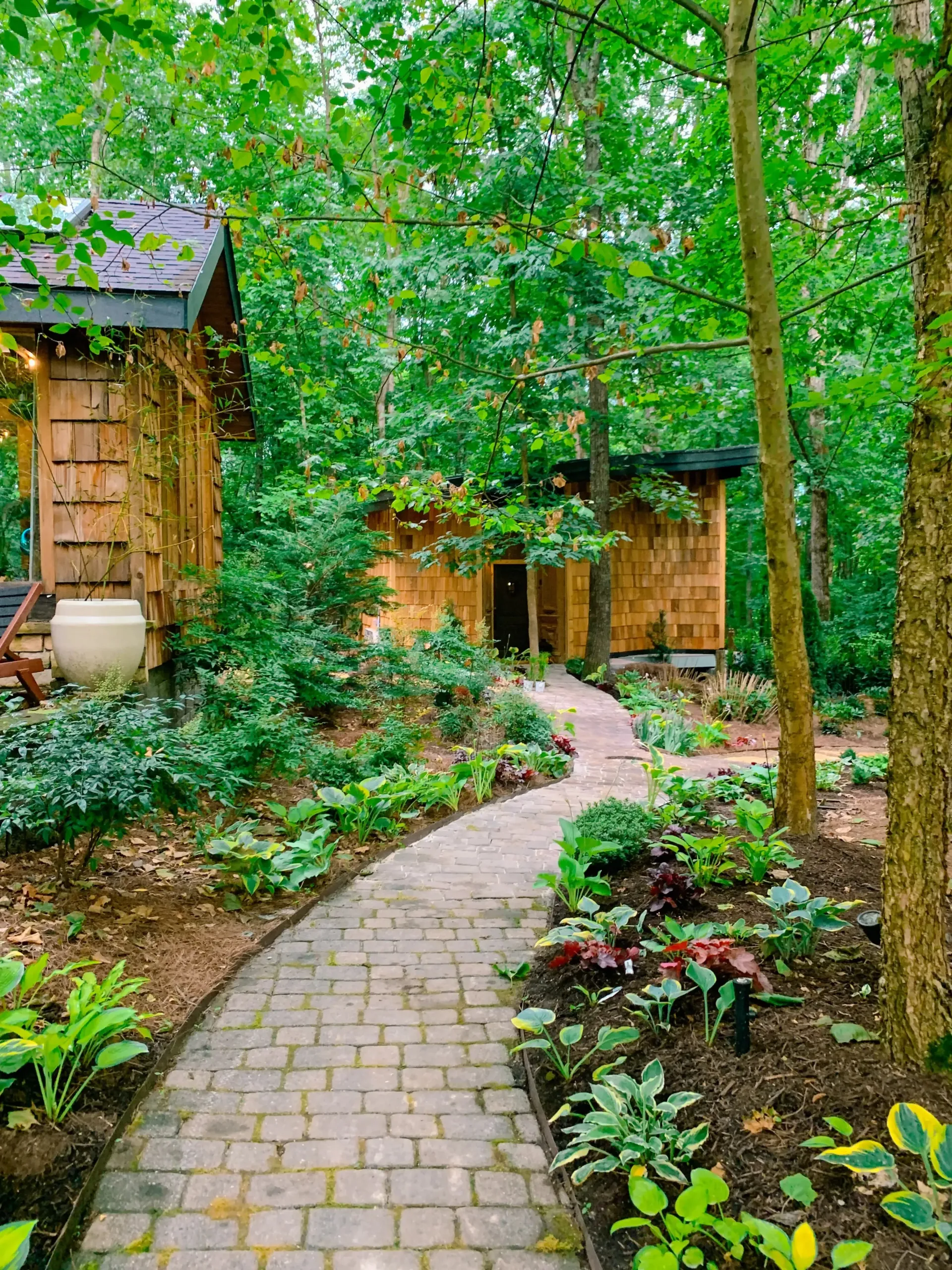 A brick walkway leading to a wooden house in the woods.