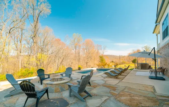 A patio with chairs , umbrellas and a fire pit in front of a house.