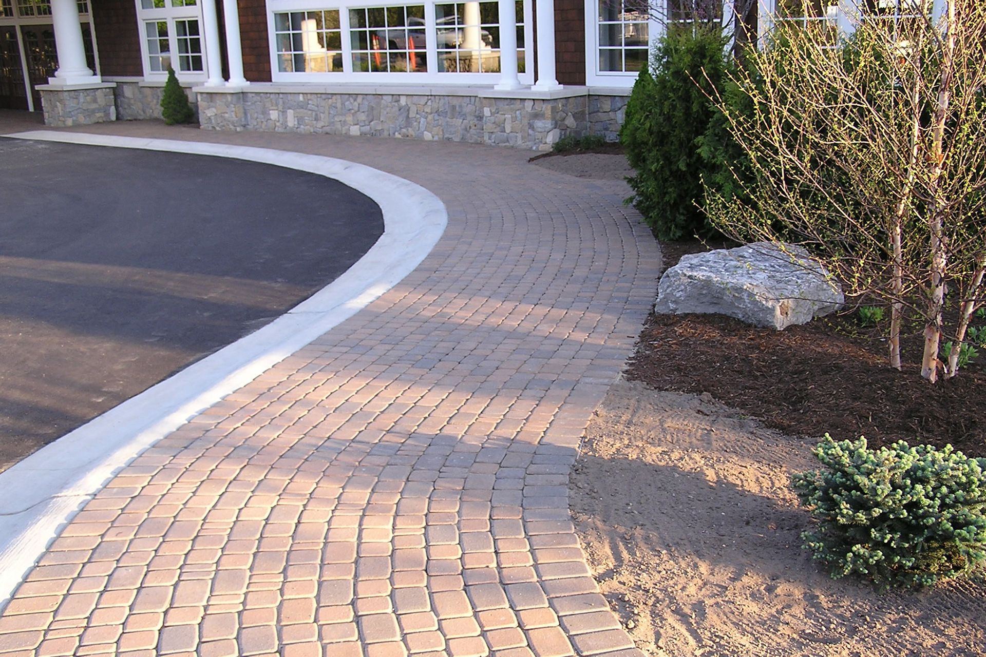 A brick walkway leading to a house with a white curb