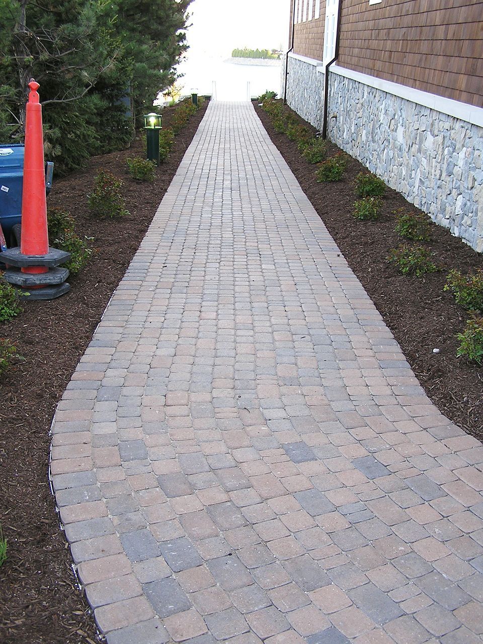 A brick walkway with a red cone on the side