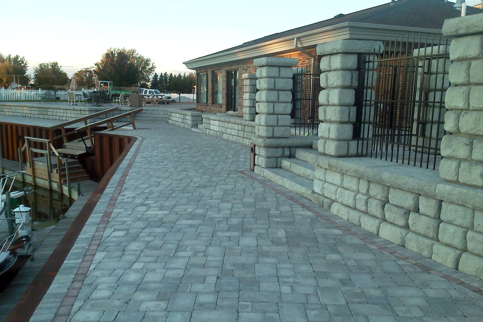 A brick walkway leading to a house with a fence