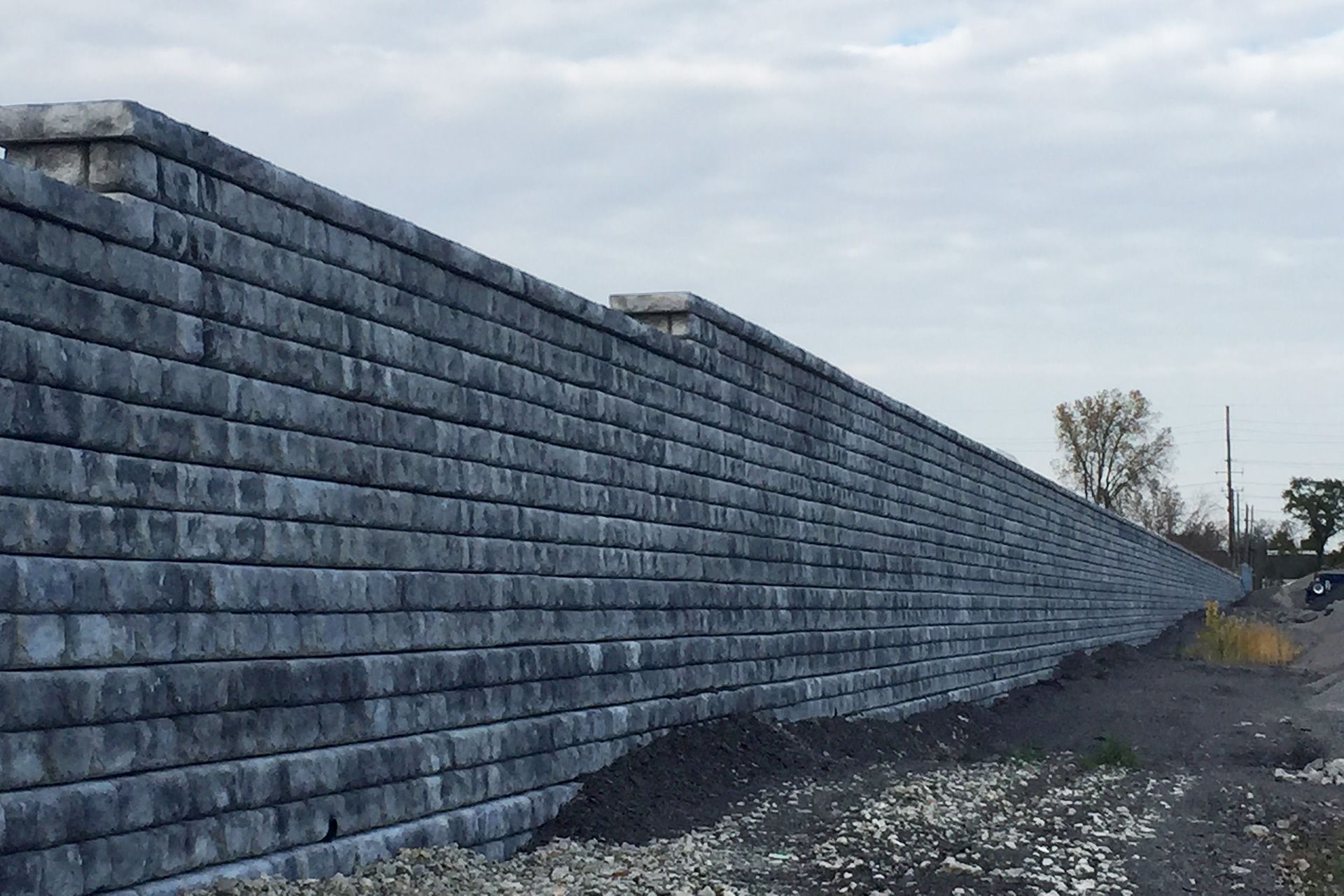 A large brick wall is sitting next to a dirt road.