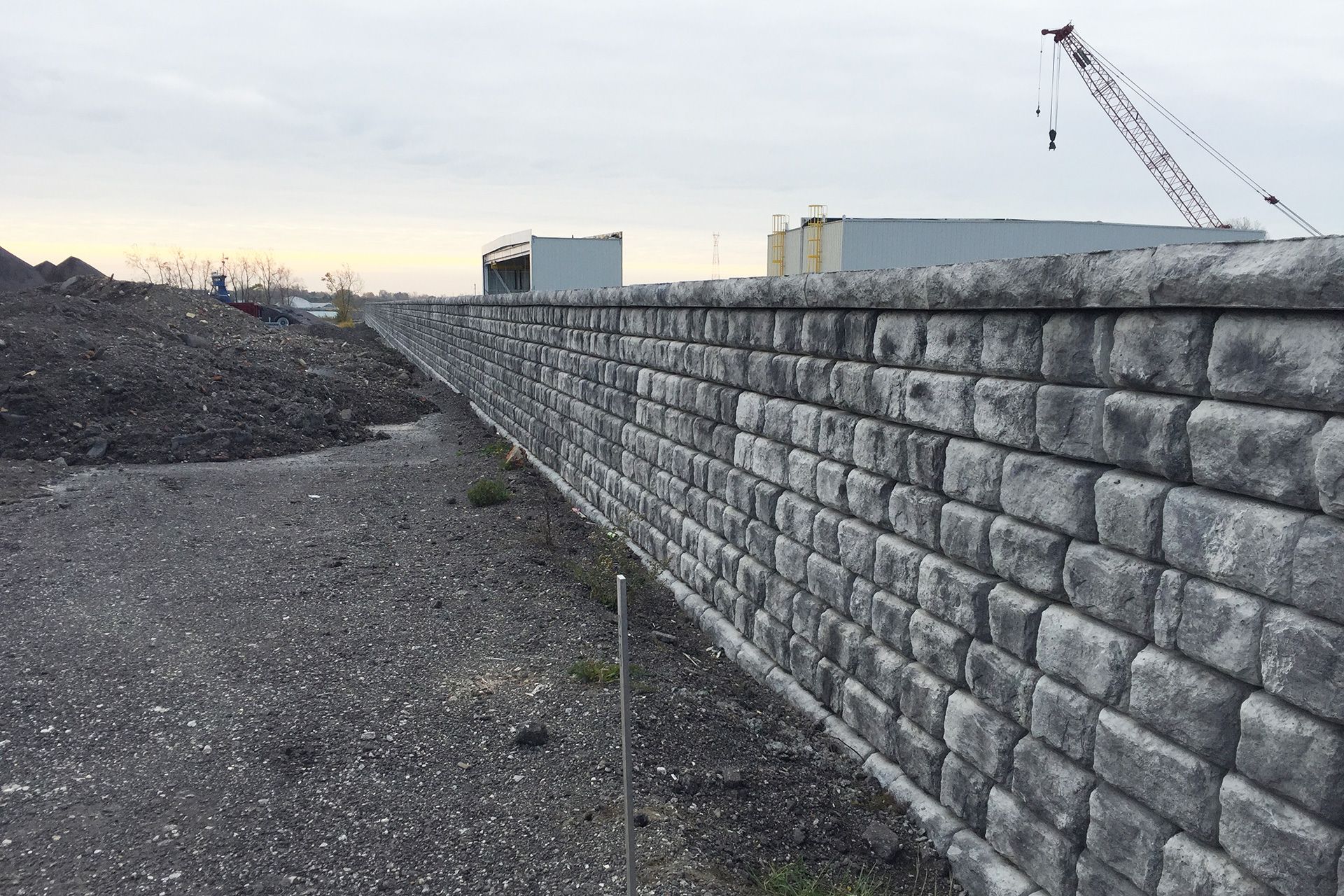 A large brick wall surrounds a gravel area with a crane in the background.
