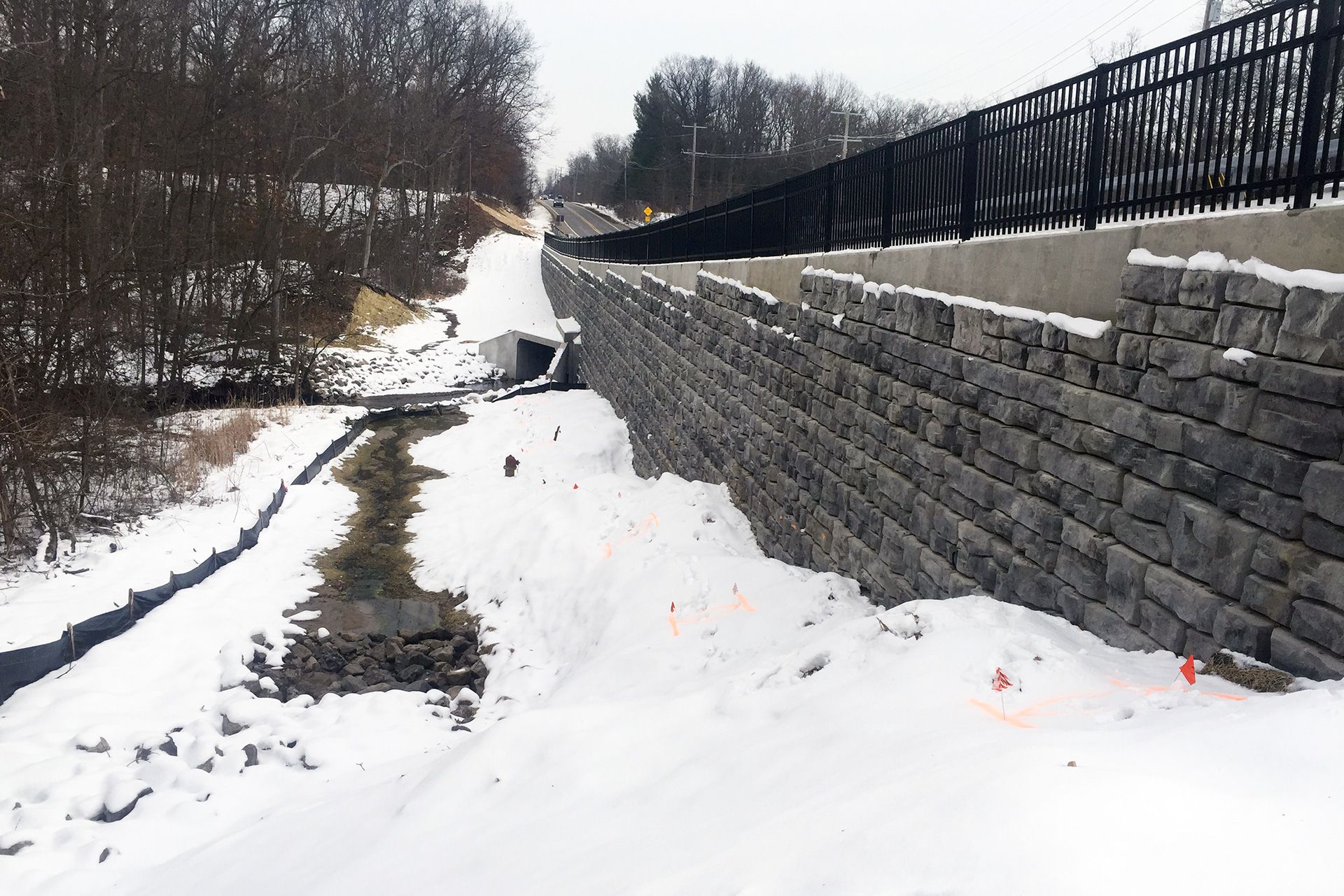 A snowy road with a stone wall and a bridge in the background
