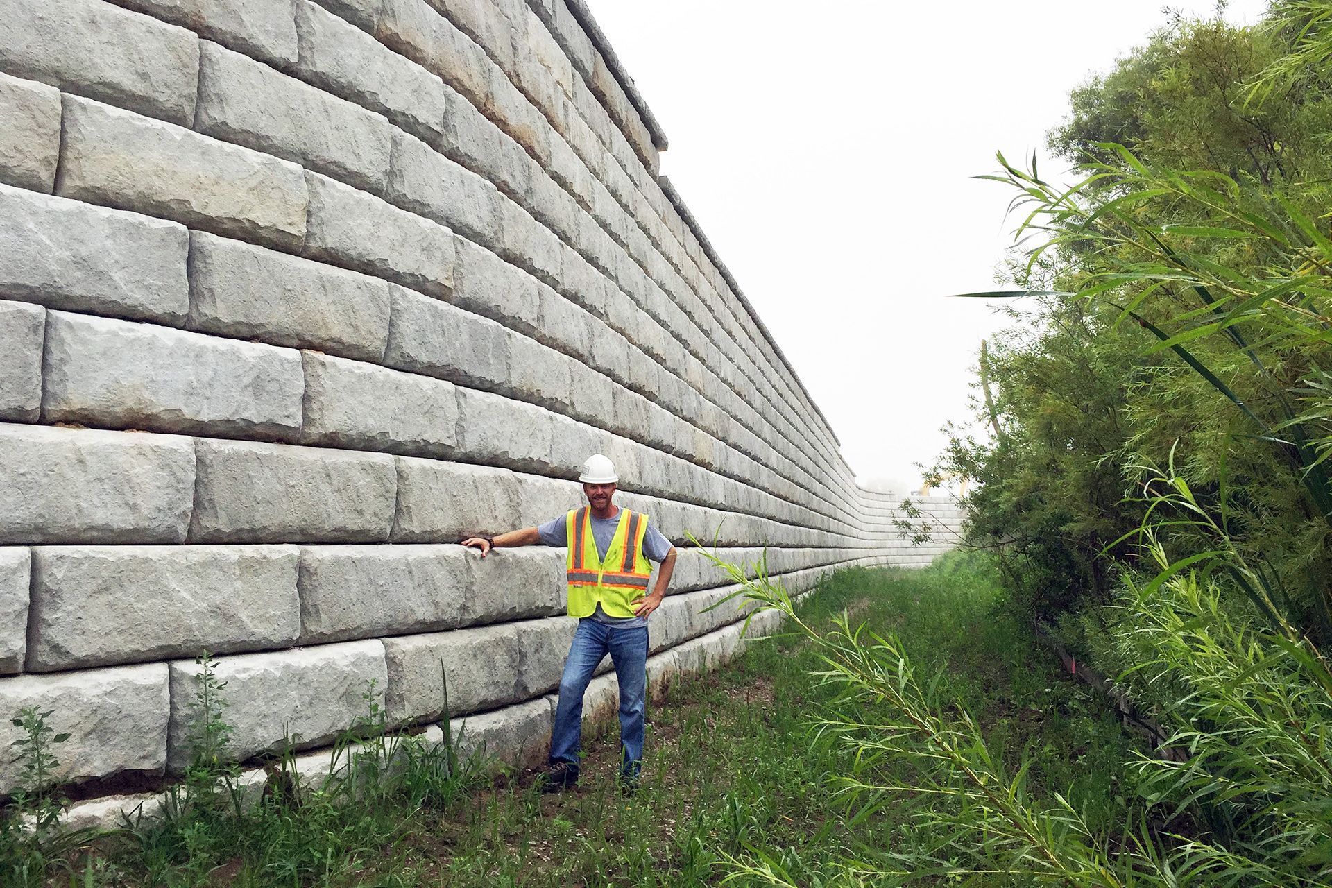 A man is standing in front of a large brick wall.