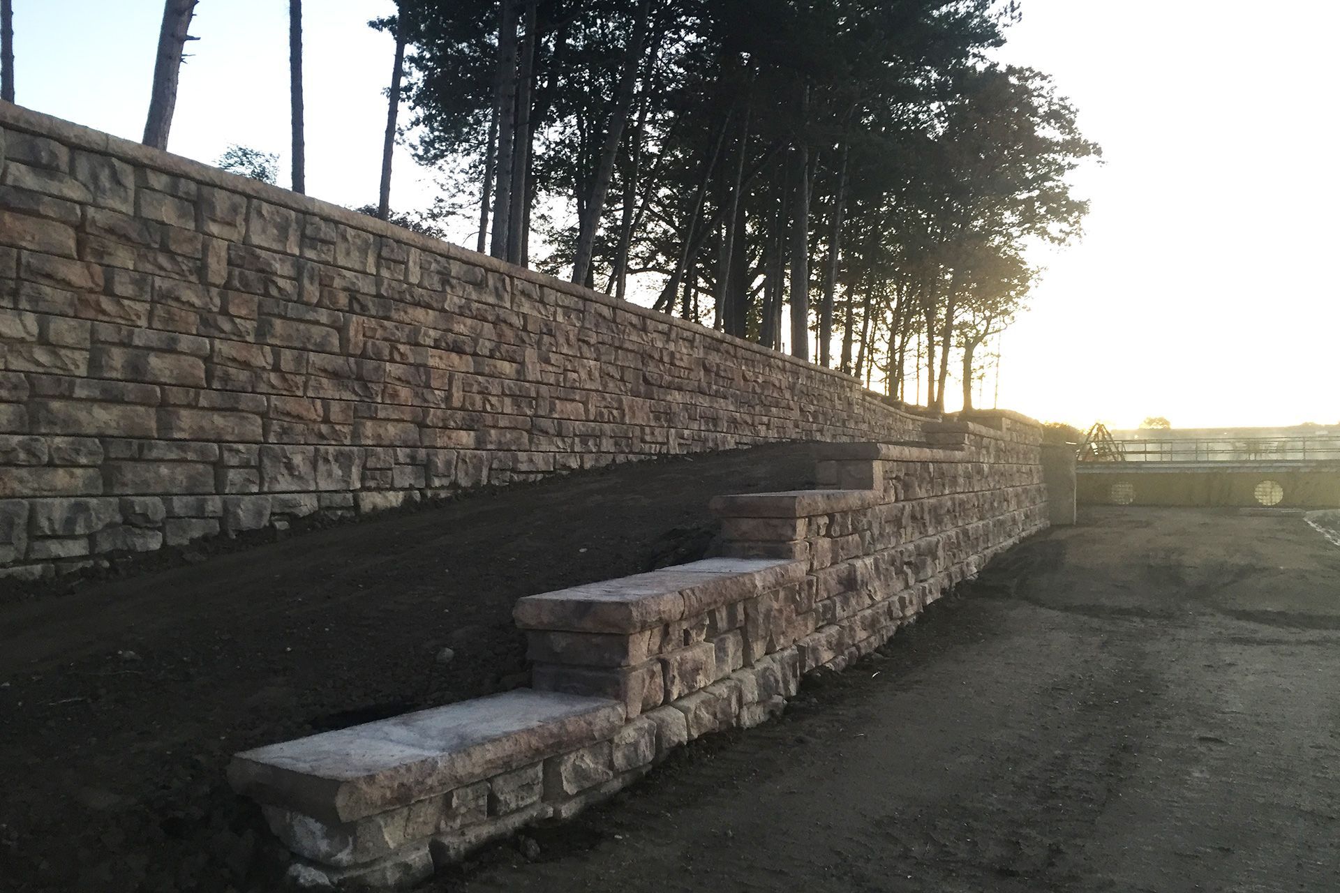 A stone wall with steps leading up to it and trees in the background