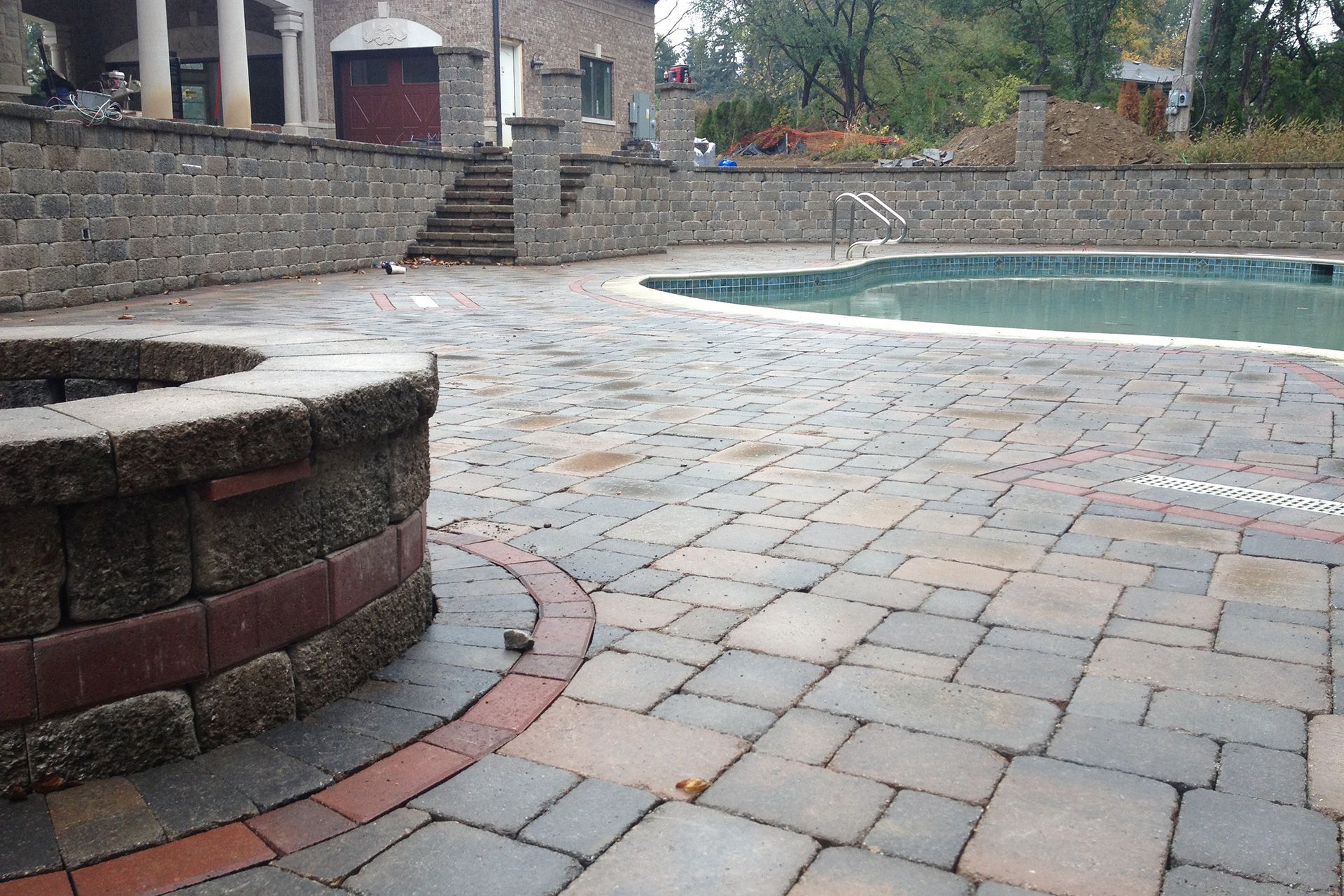 A brick patio with a fire pit and a swimming pool in the background.