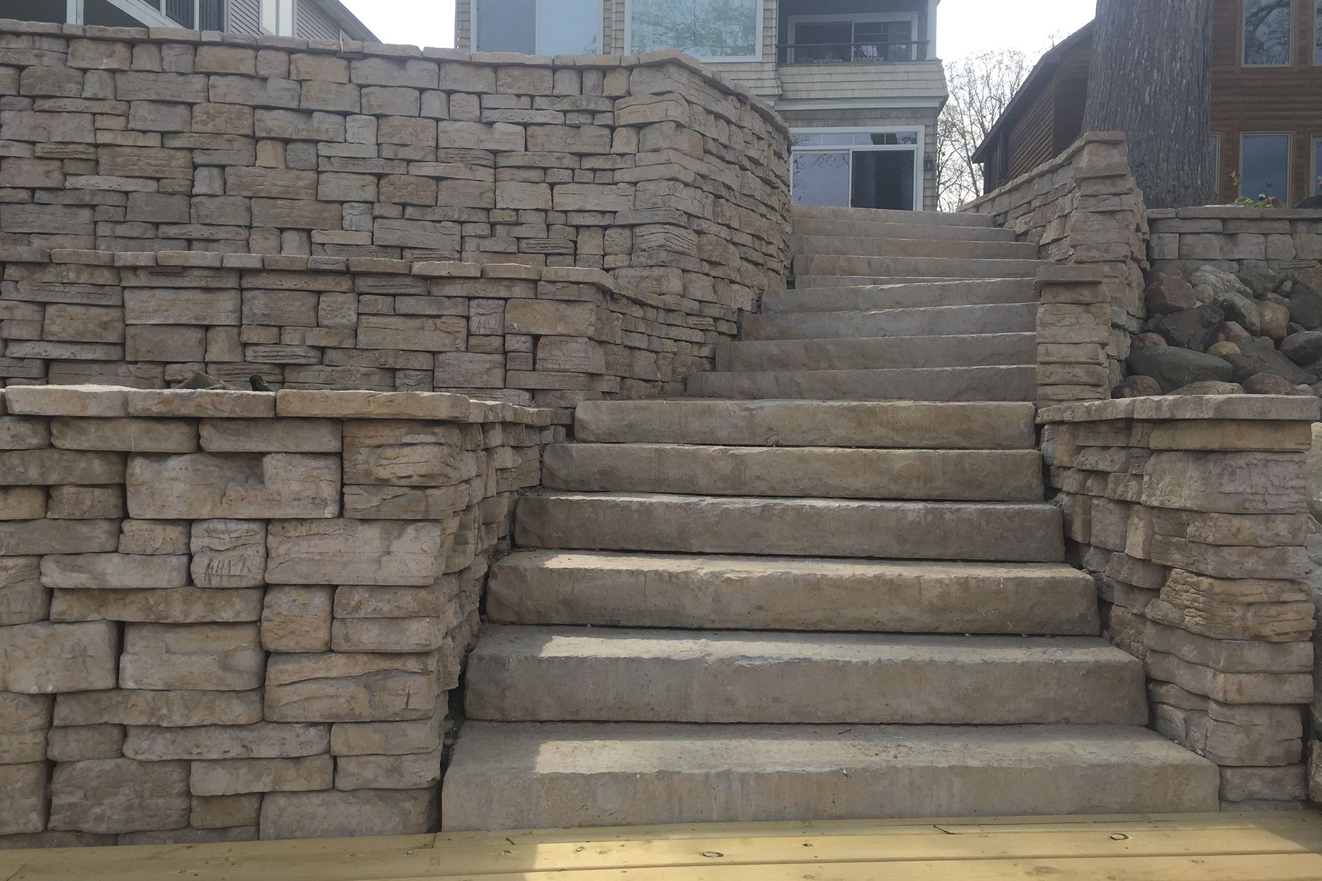 A set of stairs leading up to a house with a stone wall behind them.