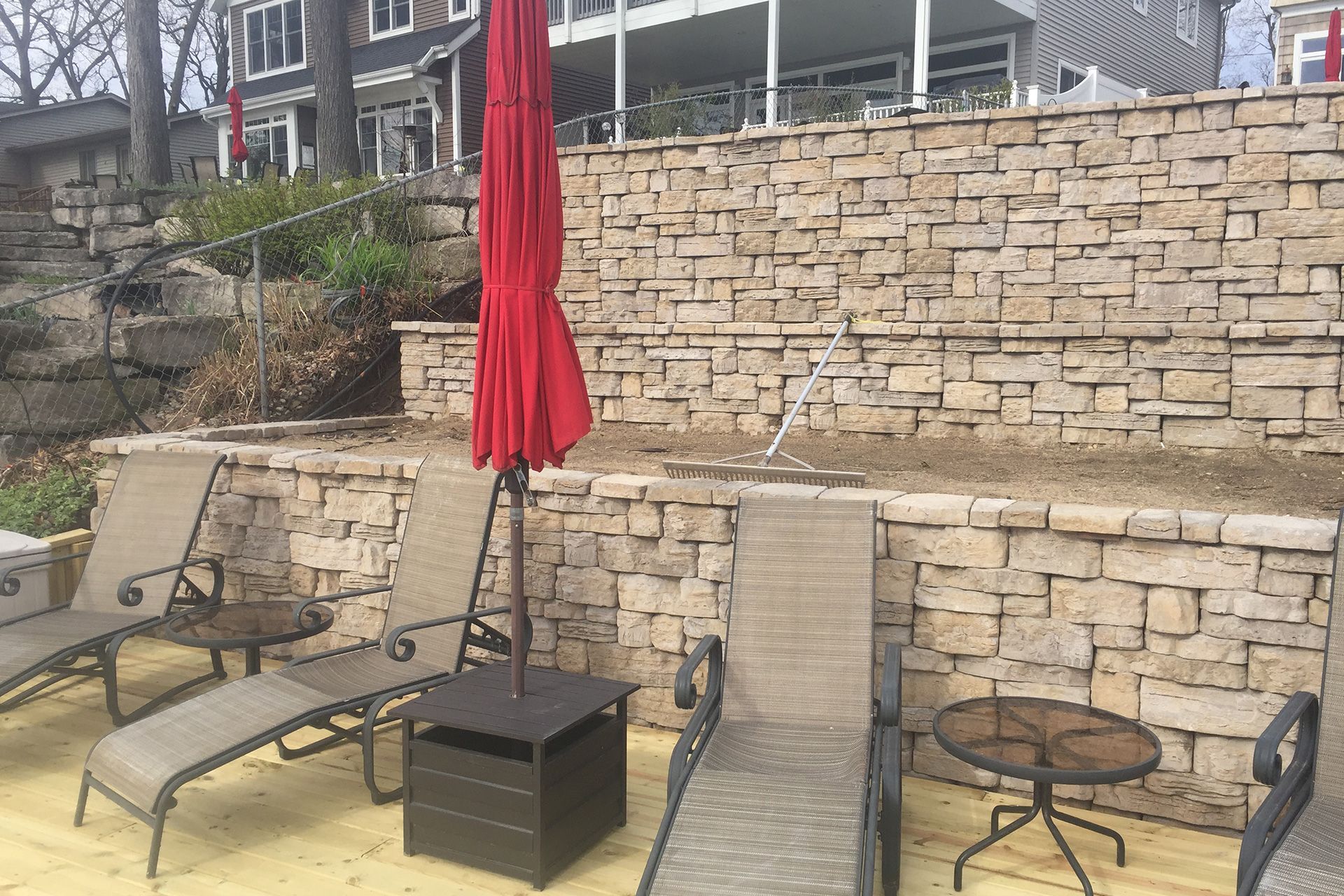 A patio with chairs , tables and an umbrella in front of a stone wall.