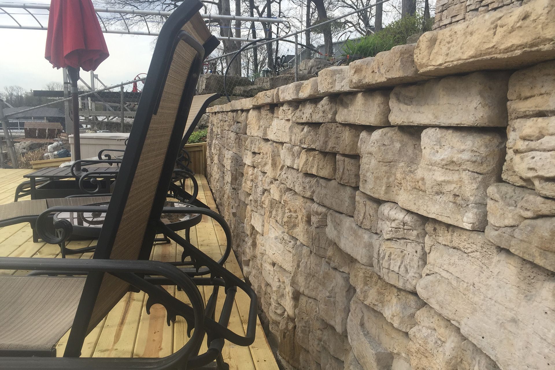 A row of rocking chairs are sitting on a wooden deck next to a stone wall.