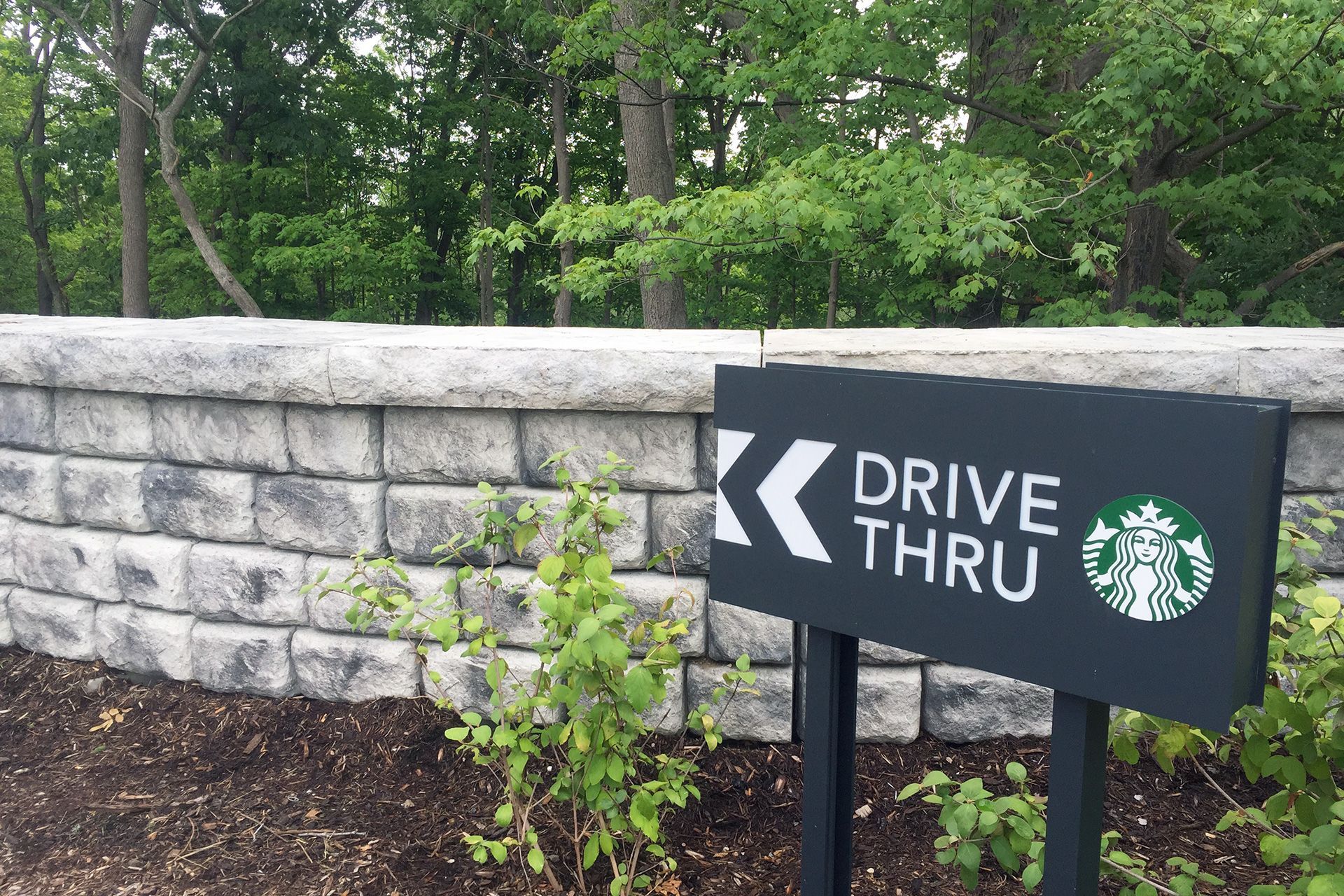 A starbucks drive thru sign is sitting in front of a brick wall.