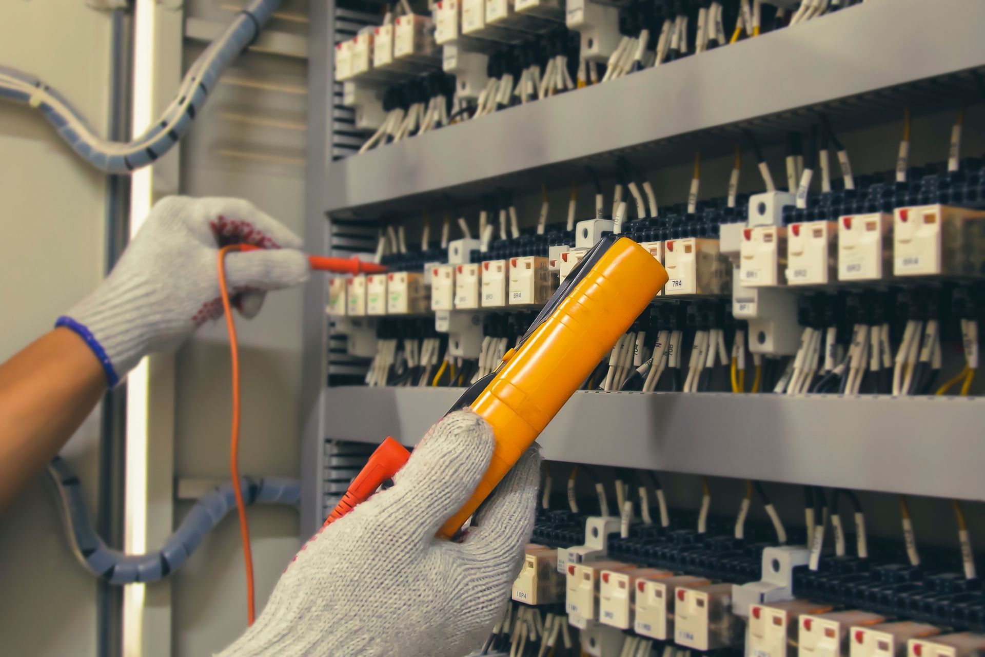Commercial electrician uses a digital multimeter to troubleshoot a complex industrial panel.