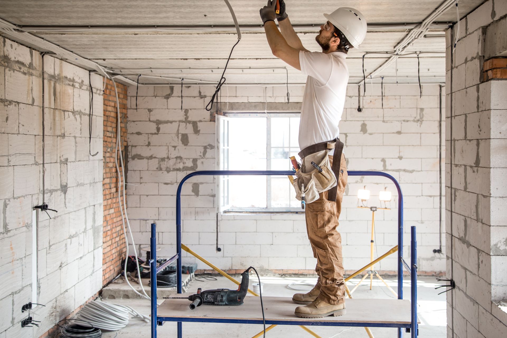 Construction worker on a scaffold, wiring ceiling in unfinished room.