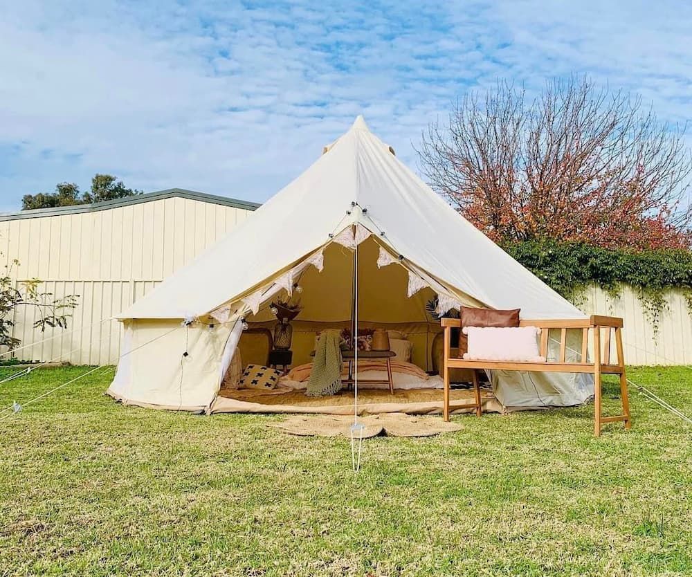 White canvas tent on a grassy lawn with a small wooden table outside under a blue sky