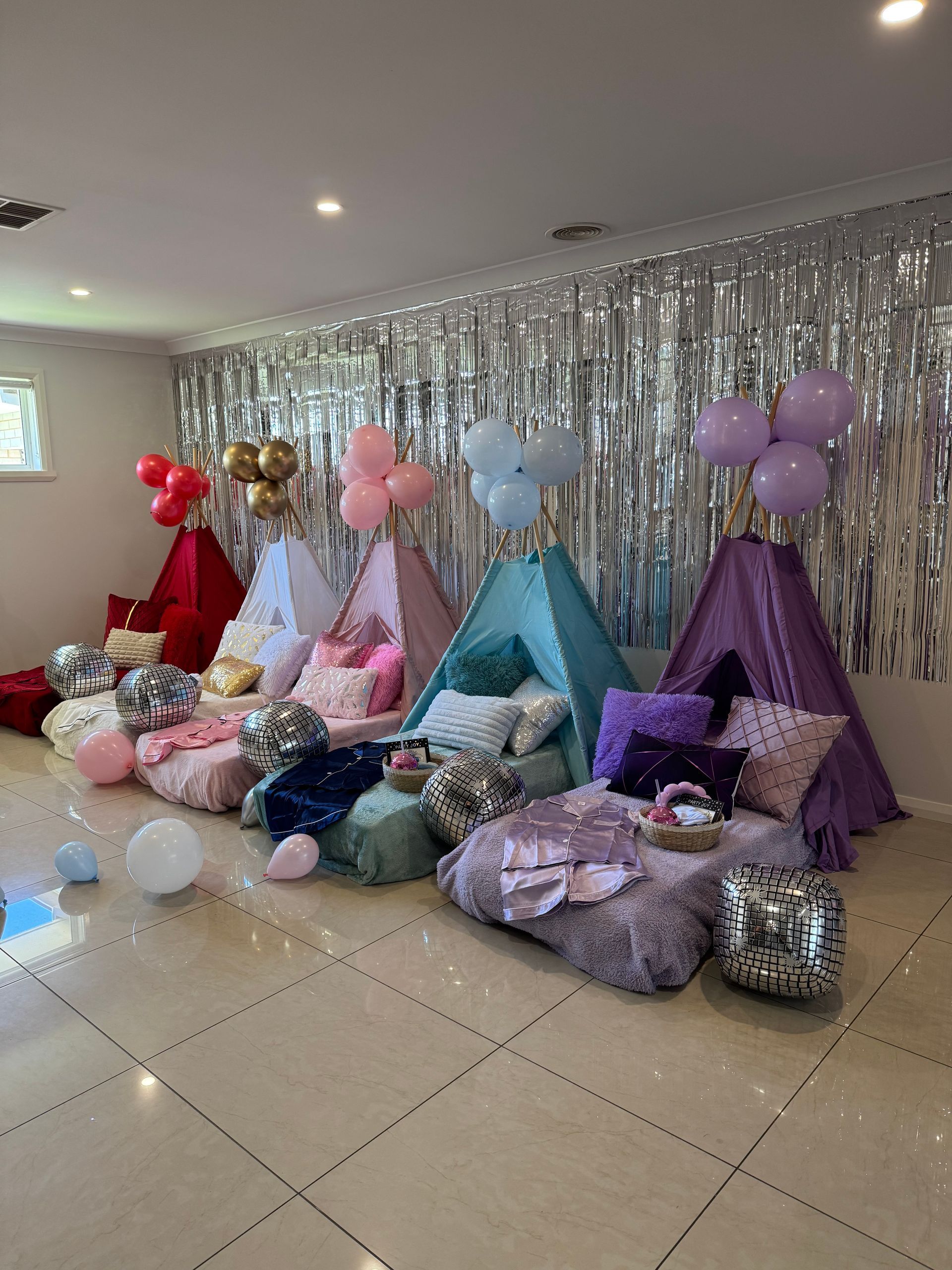 Colourful party teepees and balloons arranged against a silver tinsel backdrop in a decorated room — Sweet Parties & Braids in Tatton, NSW