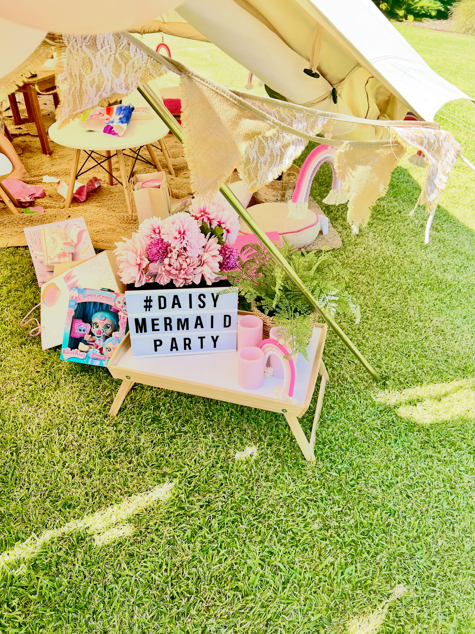 Daisy-themed market party setup with pink decor, a banner, and a small teepee on green grass.