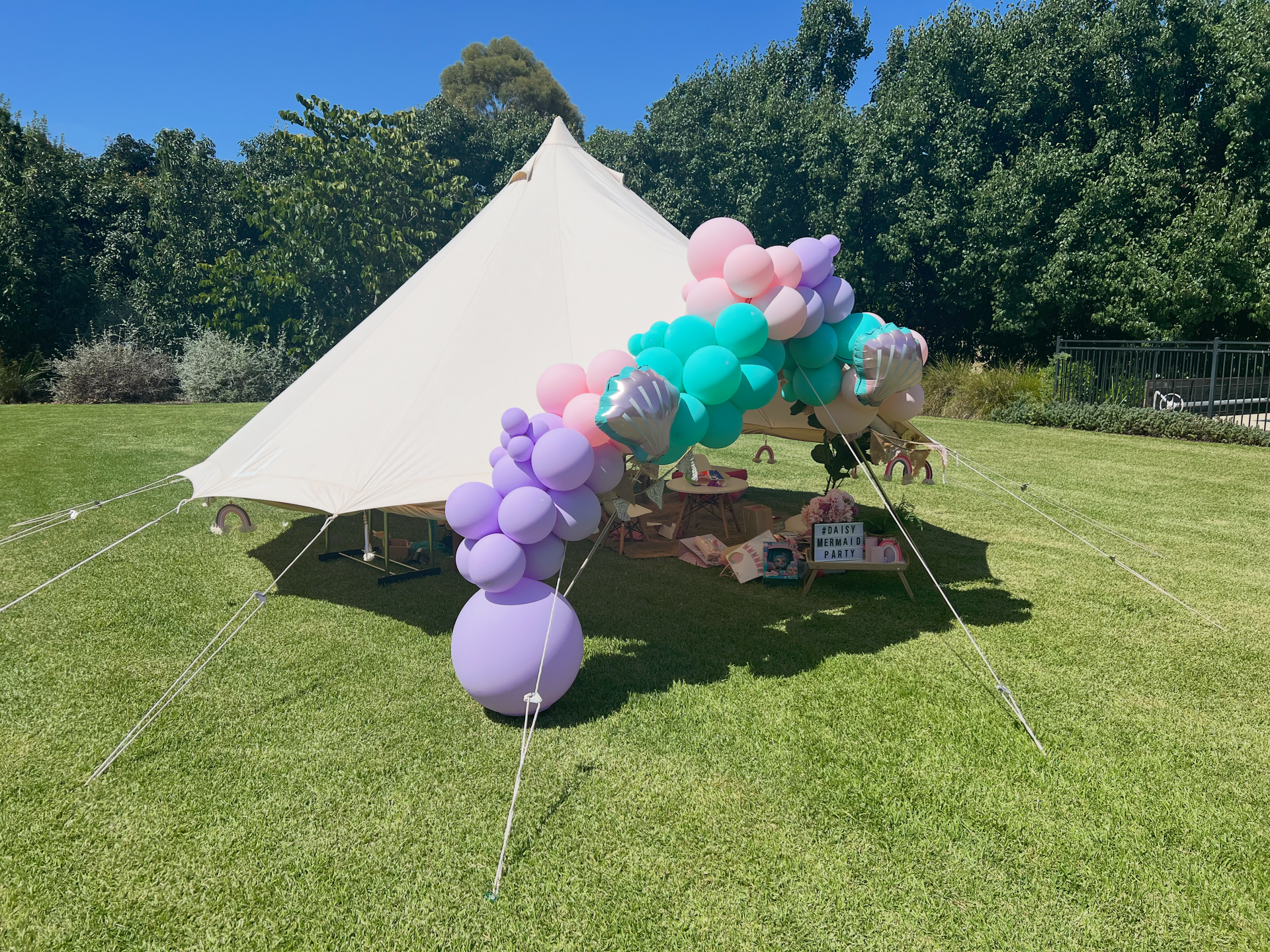 White outdoor tent decorated with pastel balloon arch on a grassy lawn