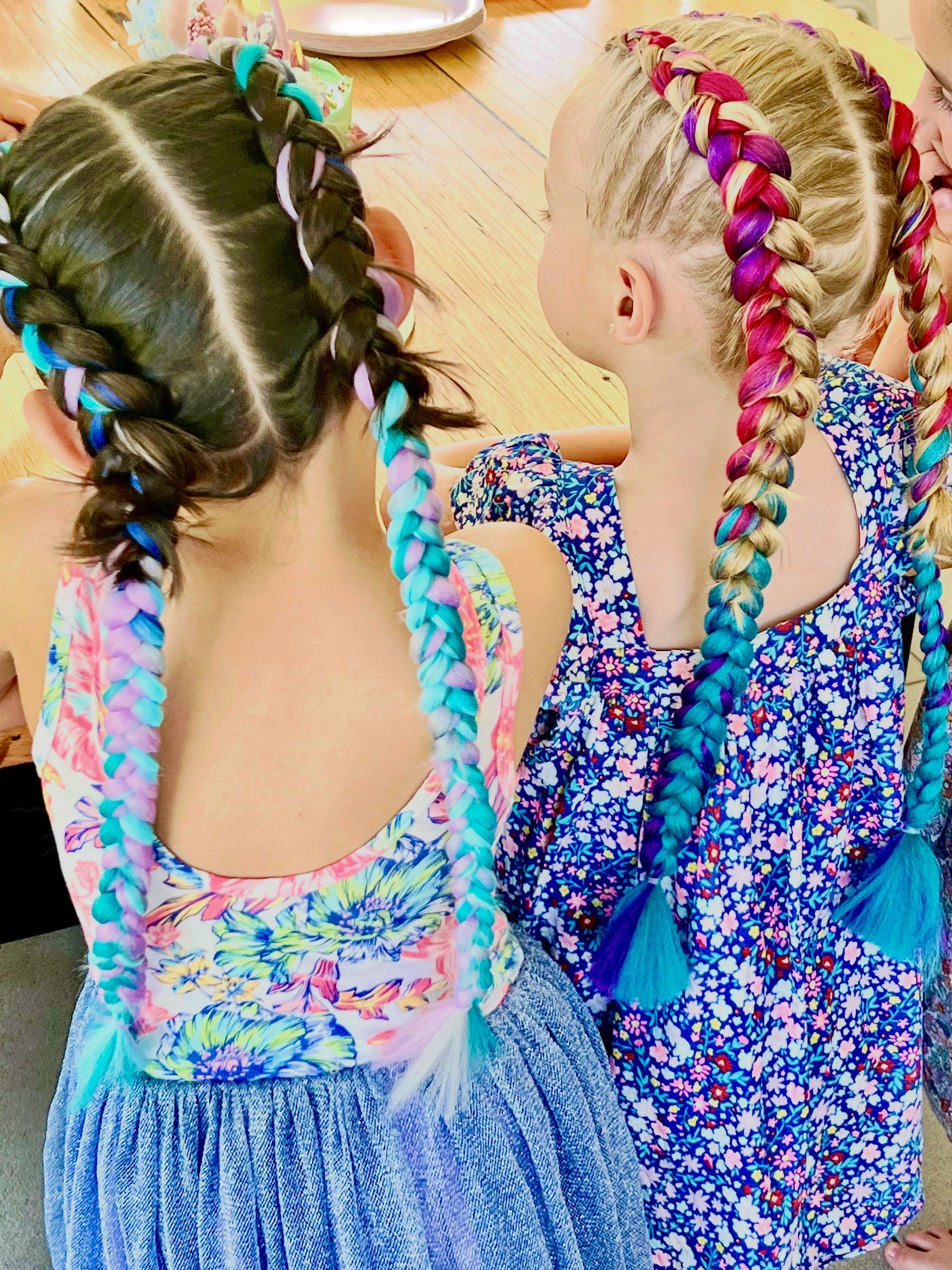 Two children with braided hair in colorful dresses sitting at a table, seen from behind β Sweet Parties & Braids in Tatton, NSW
