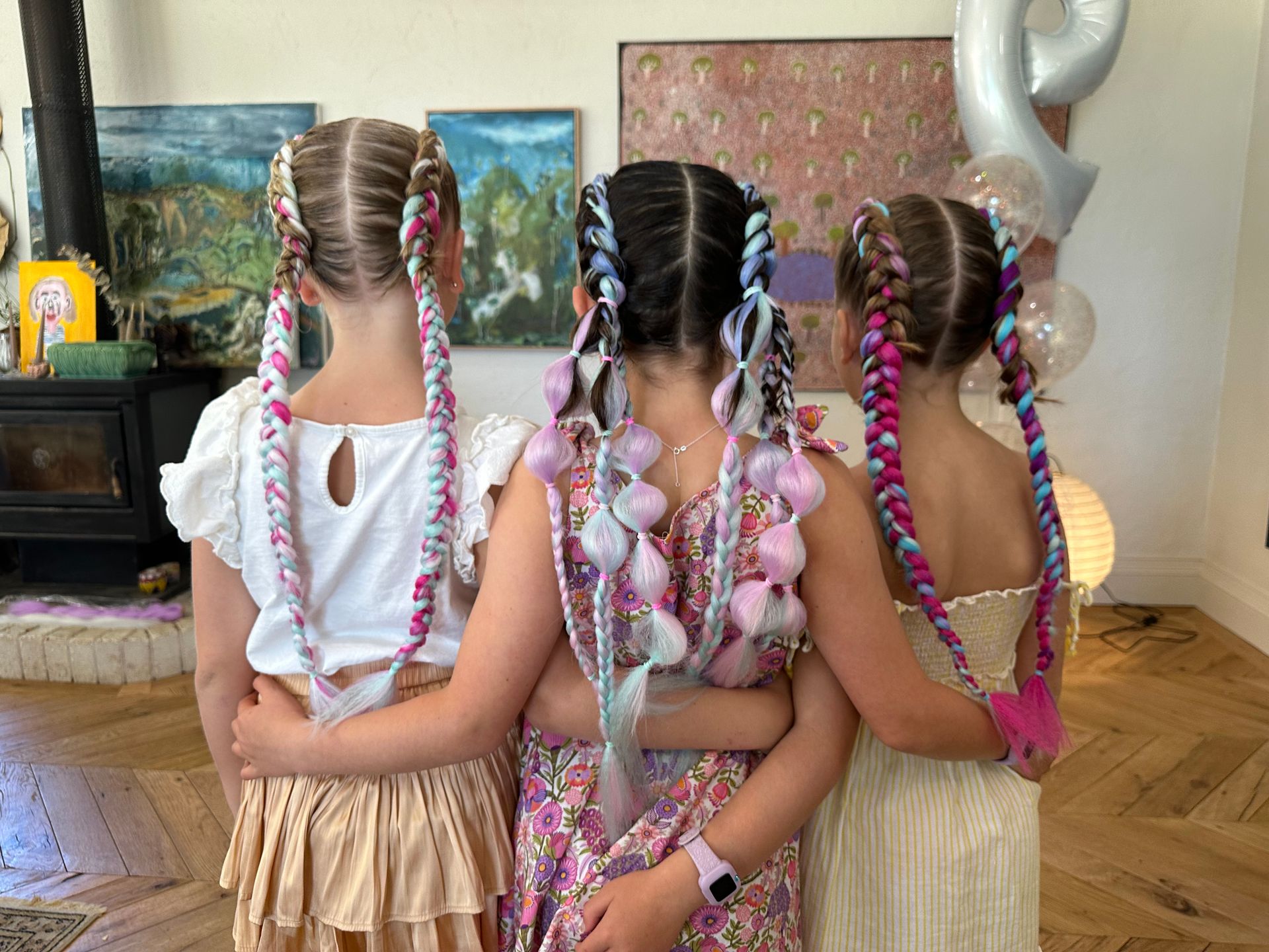 Three children with braided hair in colorful dresses stand with backs turned in a decorated room. β Sweet Parties & Braids in Tatton, NSW