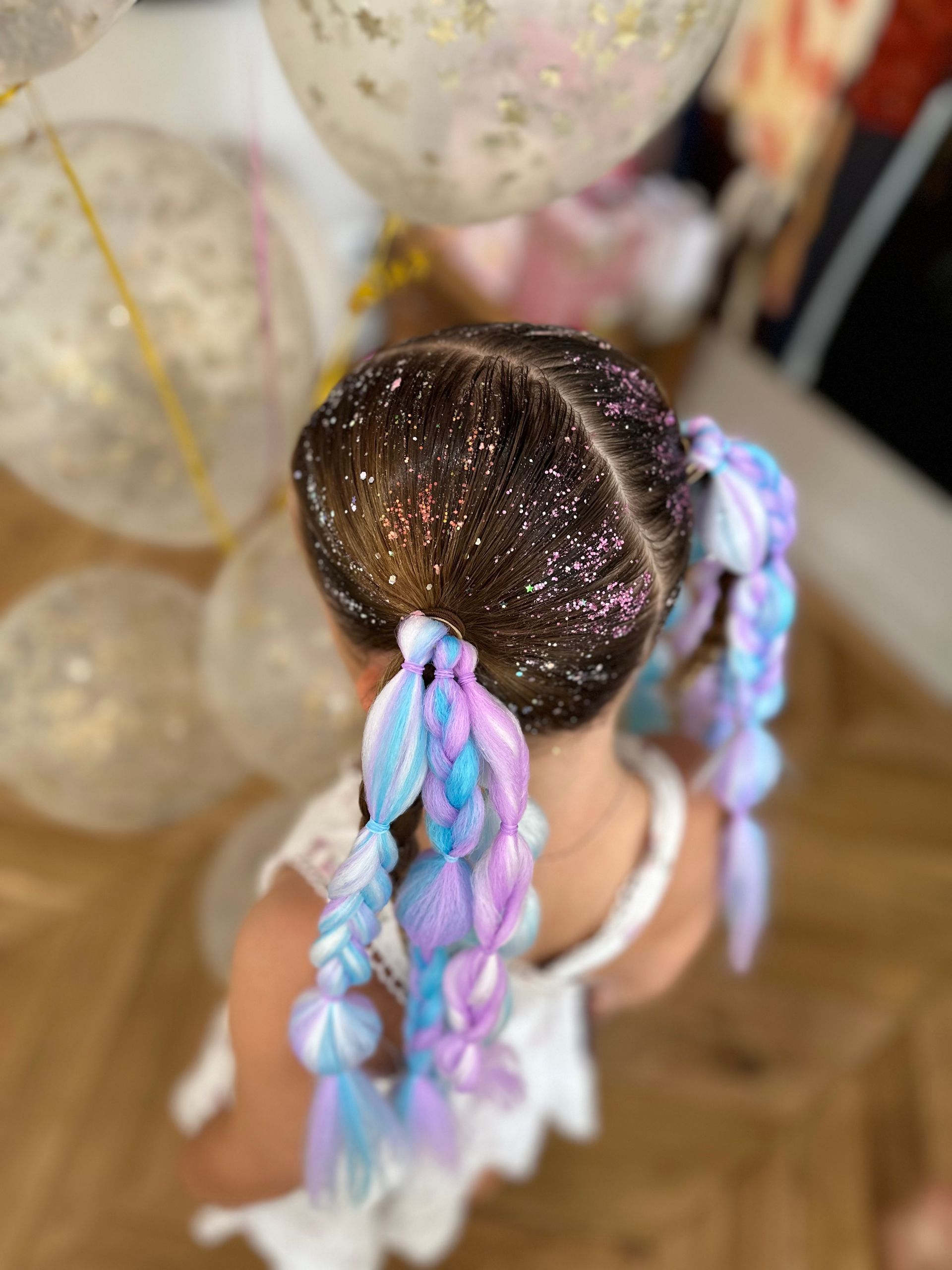 Top view of a doll with glittery hair and a pastel pink-and-blue braid on a wooden floor β Sweet Parties & Braids in Tatton, NSW